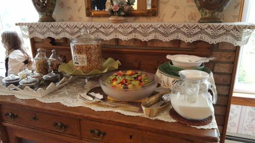 A wooden sideboard adorned with lace, featuring a fruit salad, jars of granola, and a pitcher of milk.