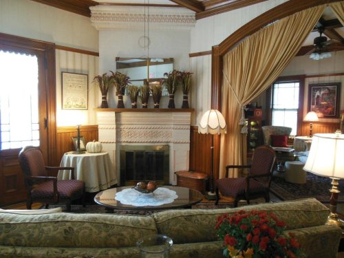 Cozy living room with a fireplace, elegant furniture, and decorative plants, featuring warm lighting and rich wood details.