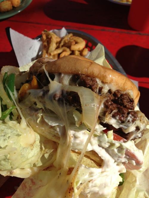 A close-up of a juicy hamburger with lettuce, onions, and creamy sauce, served with a side of fries.
