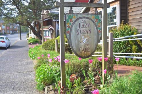 Sign for "The Lazy Susan Cafe" surrounded by colorful flowers and a quaint street scene.