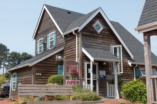 A charming wooden building with a sloped roof, blue shutters, and an "OPEN" sign, surrounded by greenery.