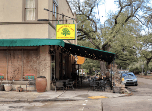 A cozy café with outdoor seating, green awning, and a sign reading "Lemon's Café" on a tree-lined street.