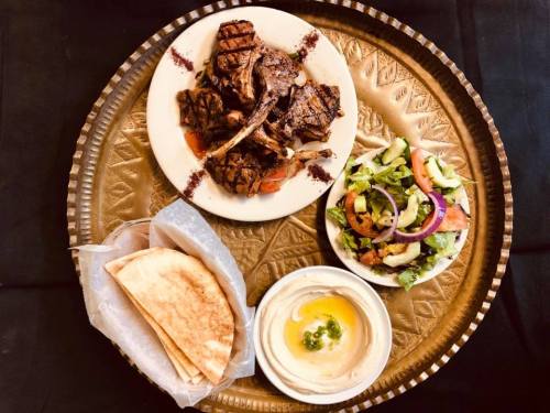 A golden tray with grilled lamb chops, a fresh salad, pita bread, and hummus, beautifully arranged.