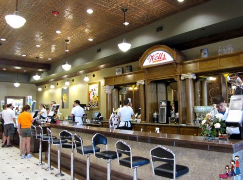 A vintage-style diner interior with a long counter, bar stools, and staff serving customers in a lively atmosphere.