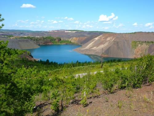 A serene landscape featuring a blue lake surrounded by rocky hills and green vegetation under a clear blue sky.