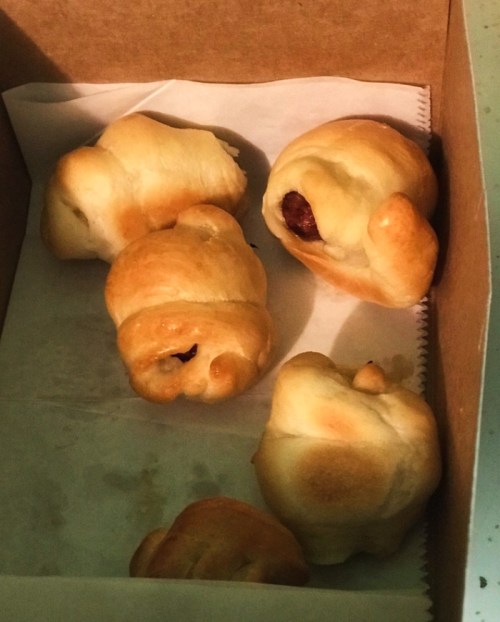 A box containing several golden-brown crescent rolls with a filling, some partially visible.