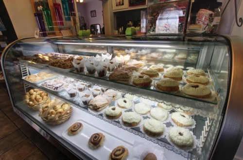 A display case filled with various baked goods, including pastries, cakes, and cookies, in a cozy bakery setting.