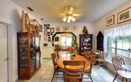 A cozy dining area with a wooden table, chairs, and decorative cabinets, surrounded by framed artwork and a bright window.