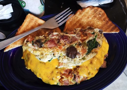 A plate with a cheesy omelette filled with vegetables and meat, served with two slices of toasted bread.