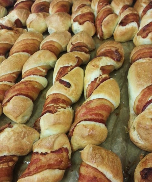 A close-up of freshly baked pastry twists wrapped in crispy bacon, arranged neatly on a baking sheet.
