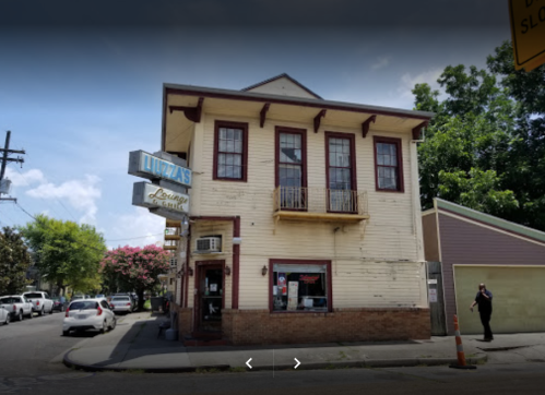 A two-story building with a sign reading "Lizza's Lounge" and a balcony, surrounded by trees and parked cars.