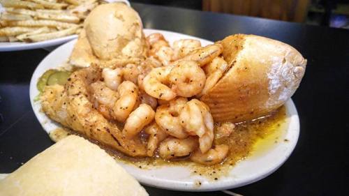 A plate featuring a shrimp po' boy sandwich with shrimp, sauce, and bread, accompanied by a side of bread rolls.