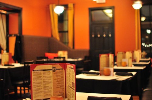 Cozy restaurant interior with tables set for dining, featuring menus and warm orange walls.