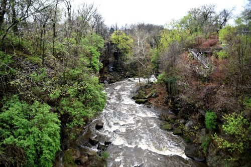 A winding river flows through a lush, green landscape with trees and rocky banks under a cloudy sky.