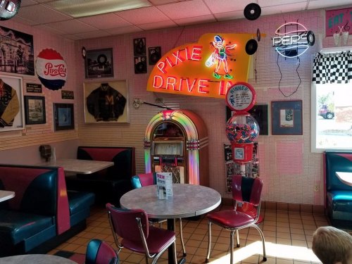A retro diner interior featuring a jukebox, gumball machine, and vintage decor with colorful seating.