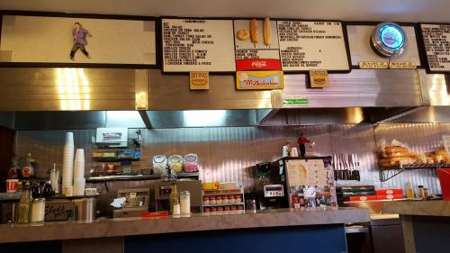 A retro diner counter with a menu board, condiments, and a display of sandwiches and drinks.