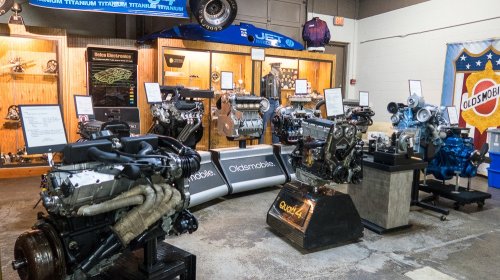 A display of various automobile engines in a museum setting, featuring Oldsmobile and other engine models.