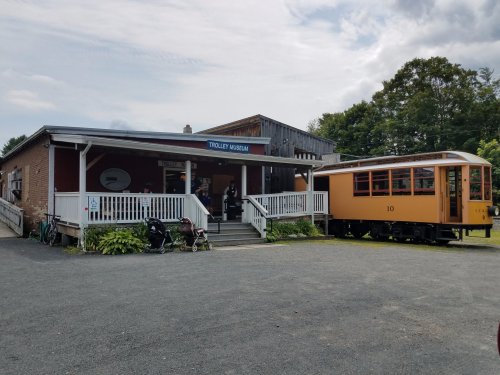 A vintage trolley parked outside the Trolley Museum, featuring a wooden building and visitors in the foreground.