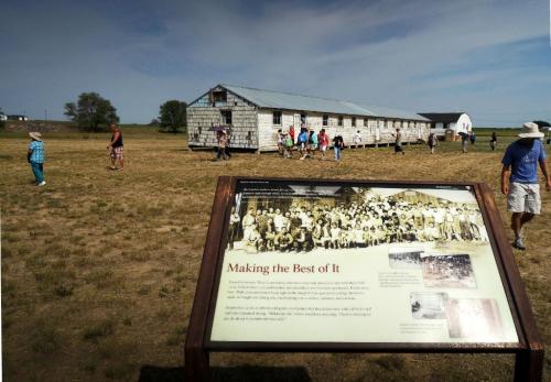 A historical site with a large building and a sign about its history, surrounded by visitors on a sunny day.