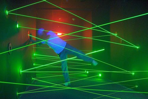 A person navigates through a room filled with green laser beams, trying to avoid touching them.