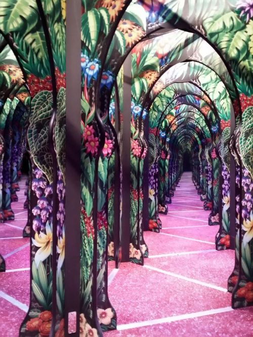 A vibrant, colorful maze of floral-patterned arches leading into a pink-tiled pathway.