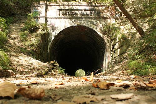 A dark, abandoned tunnel entrance surrounded by trees and fallen leaves, with "Woodville" inscribed above.