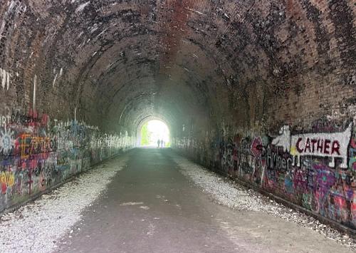 A dark tunnel with colorful graffiti on the walls, leading to a bright exit in the distance.