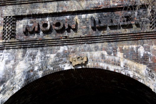 Weathered brick archway with the word "MOON" prominently displayed above, showcasing aged textures and details.