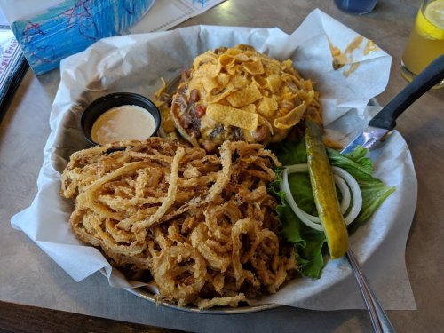 A plate featuring a burger topped with chips, onion rings, a pickle, and lettuce, served with a dipping sauce.