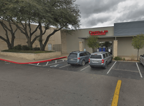 Exterior view of a building with a sign reading "DARTemUP," surrounded by trees and parked cars. Overcast sky.