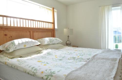 Bright bedroom with a wooden headboard, floral bedding, and a lamp beside a window with sheer curtains.