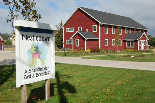 A red Scandinavian-style bed and breakfast building with a sign reading "Nestledown" in a green landscape.