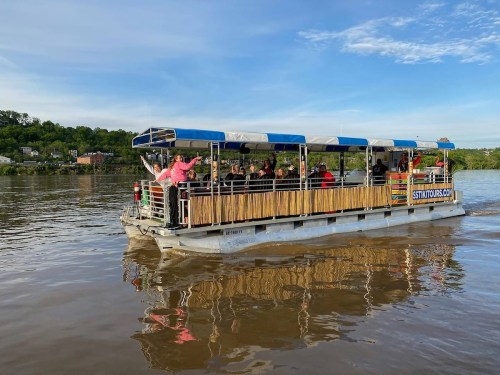 A tour boat with passengers enjoying a scenic ride on a river, surrounded by greenery and a clear blue sky.