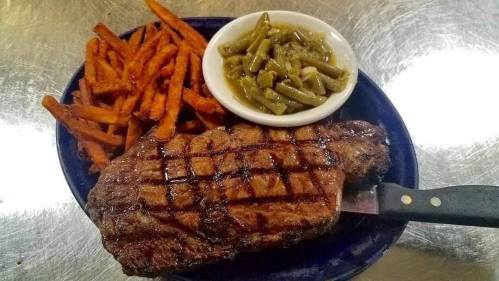 A grilled steak with a crosshatch pattern, served with sweet potato fries and green beans on a blue plate.