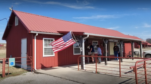 A red building with a metal roof, featuring a U.S. flag, with people gathered outside.