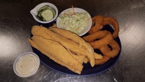 A plate of fried fish fillets, onion rings, coleslaw, and pickles, served with a dipping sauce.