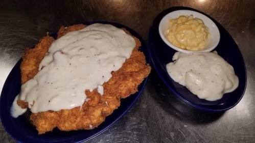 A plate of fried chicken smothered in white gravy, accompanied by two sides: creamy macaroni and cheese and mashed potatoes.
