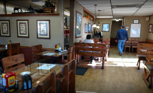 A cozy diner interior with wooden benches, tables, and decor, featuring patrons and a person walking towards the back.