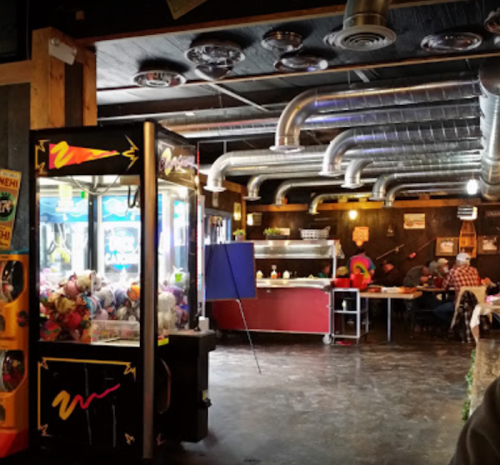 Interior of a casual eatery featuring a claw machine, dining area, and exposed metal ductwork.
