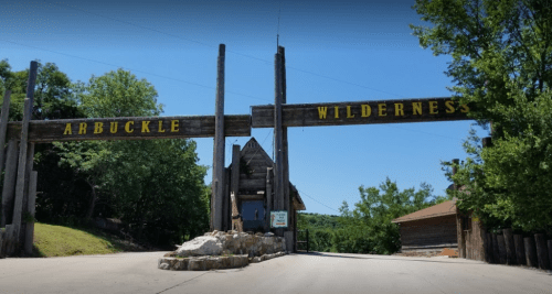 Entrance to Arbuckle Wilderness, featuring a wooden archway and lush greenery under a clear blue sky.