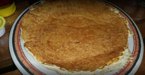 A large, golden-brown pancake on a decorative plate, resting on a wooden table.