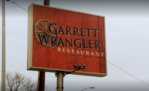 Sign for Garrett Wrangler Restaurant, featuring a wagon wheel design and text indicating breakfast, lunch, and dinner.