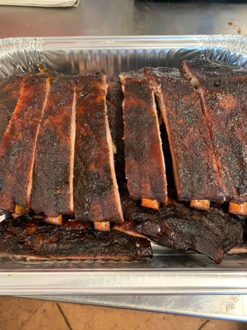 A tray of perfectly cooked, smoky barbecue ribs, sliced and ready to serve.