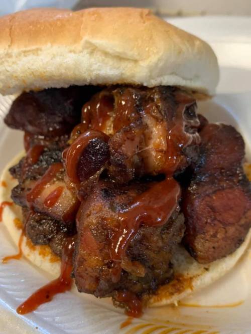A close-up of a sandwich filled with tender, smoky meat and drizzled with barbecue sauce, served on a soft bun.