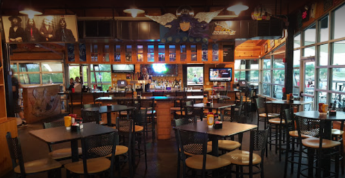 Interior of a bar with tables, a long counter, and large windows, featuring a rock-themed decor and a vibrant atmosphere.
