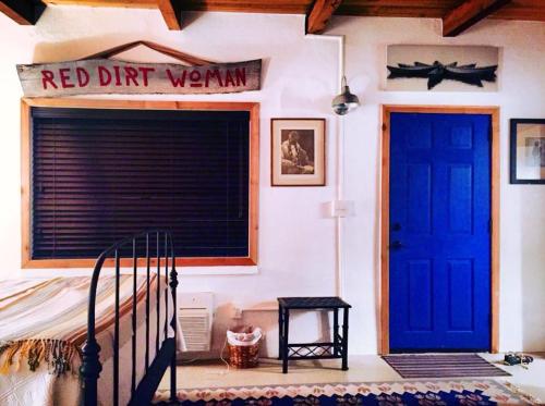 Cozy room featuring a blue door, wooden sign reading "RED DIRT WOMAN," and a bed with a patterned blanket.