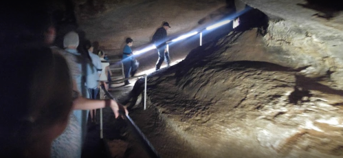 A group of people walking through a dimly lit cave, with a light illuminating the rocky path ahead.