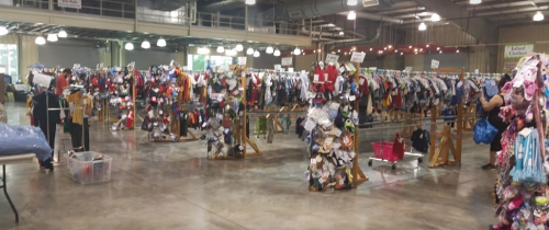 A large indoor space filled with racks of colorful clothing and accessories for sale, with shoppers browsing.