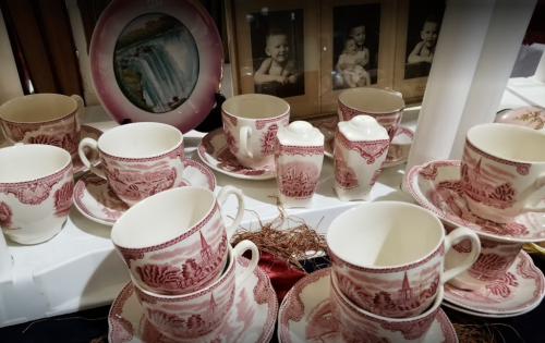 A collection of vintage pink and white china teacups, saucers, and a sugar bowl displayed with old photographs.