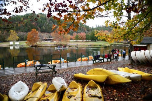 A serene lake surrounded by autumn foliage, with kayaks on the shore and people enjoying the scenery.